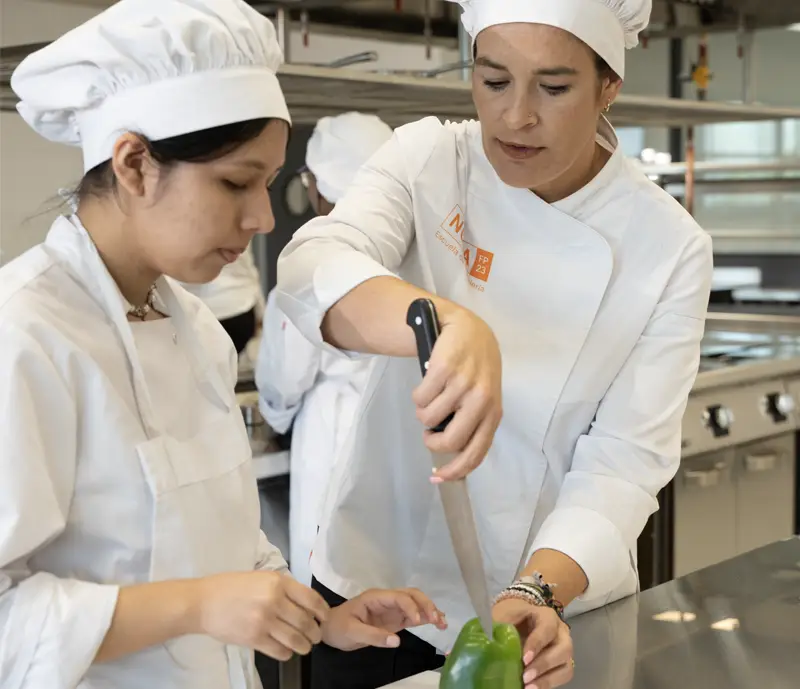 Profesora de cocina instruyendo a una alumna en el proceso formativo del centro de formación profesional Nova FP23 en Madrid.