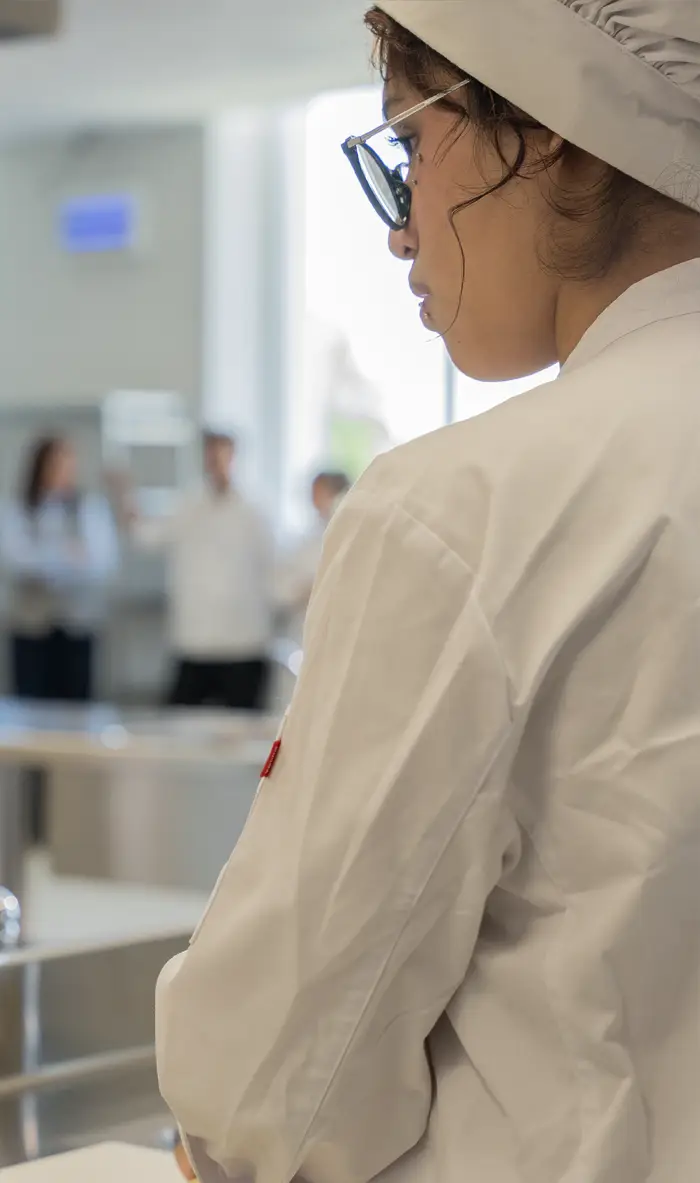 Alumna de grado medio en hostelería equipada con uniforme de cocina durante las clases prácticas en el centro Nova FP23 en Madrid.