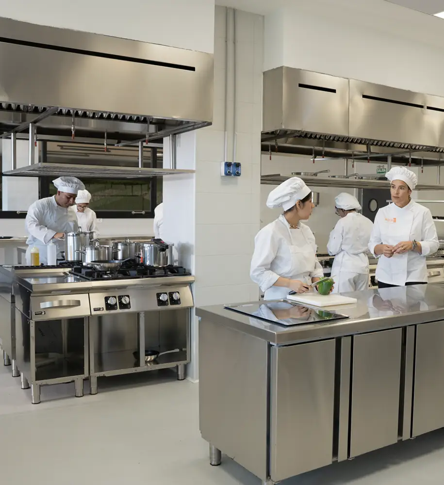 Profesores y alumnos trabajando en la cocina industrial de la Escuela de Hostelería Nova FP23 durante una clase práctica en Madrid.